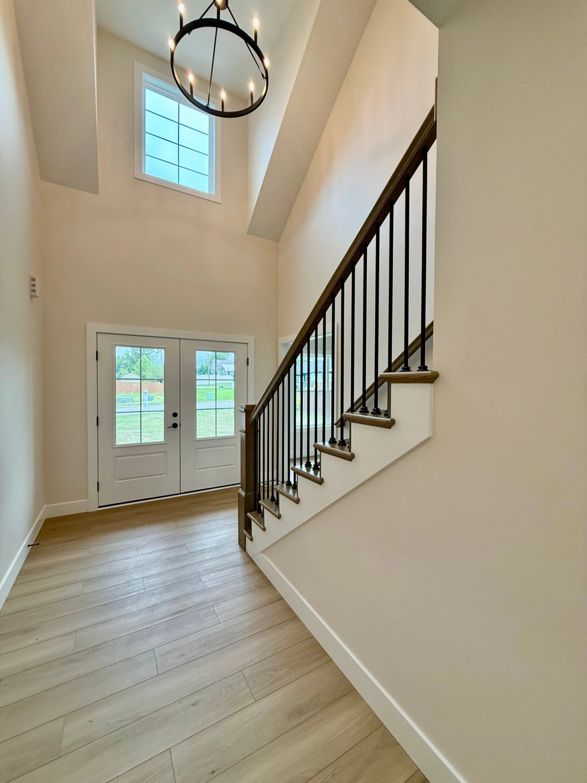 Sterchi Homes entryway featuring wood staircase, black metal balusters, high ceiling, chandelier, and natural light.