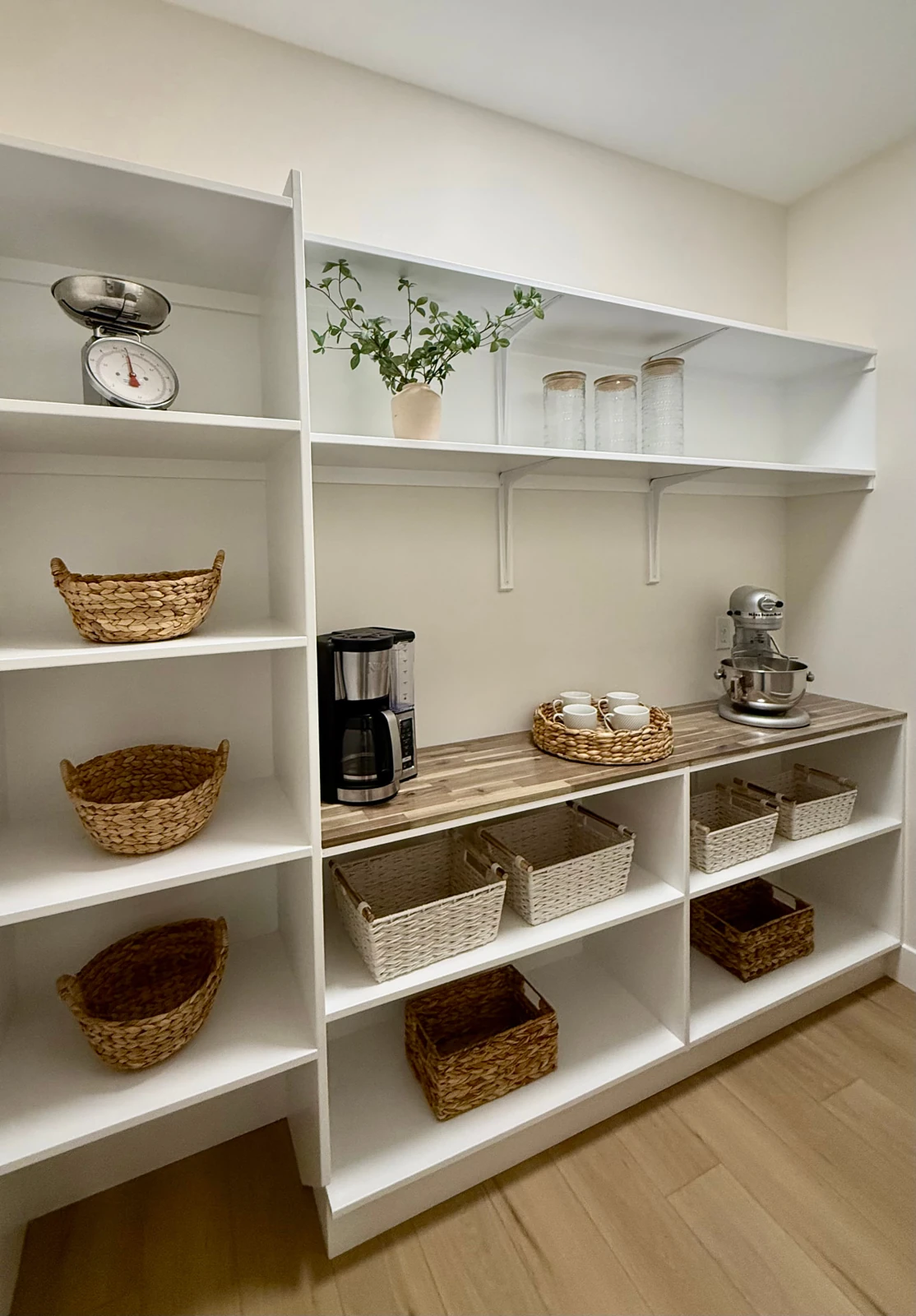 Sterchi Homes walk-through pantry with open white shelving, countertop workspace, woven storage baskets, and small appliances.