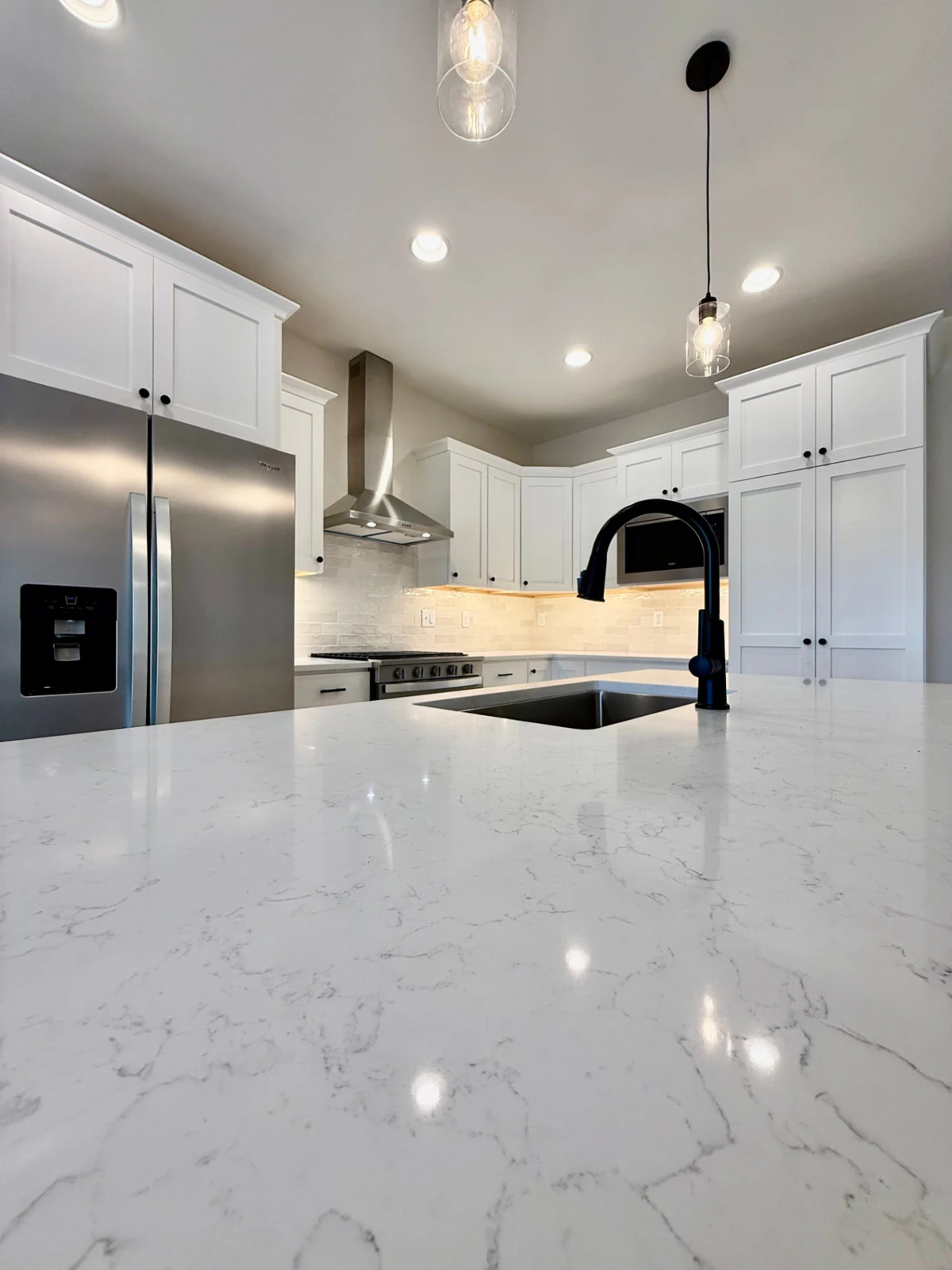 Sterchi Homes kitchen with white cabinetry, light veined countertops, stainless appliances, and contrasting black fixtures.