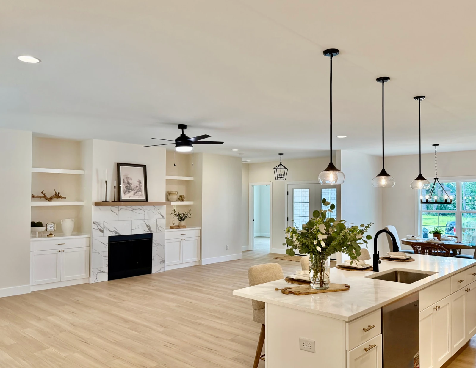 Sterchi Homes open-concept kitchen and living area featuring a fireplace, built-in cabinetry, light wood-look flooring, and pendant lighting.