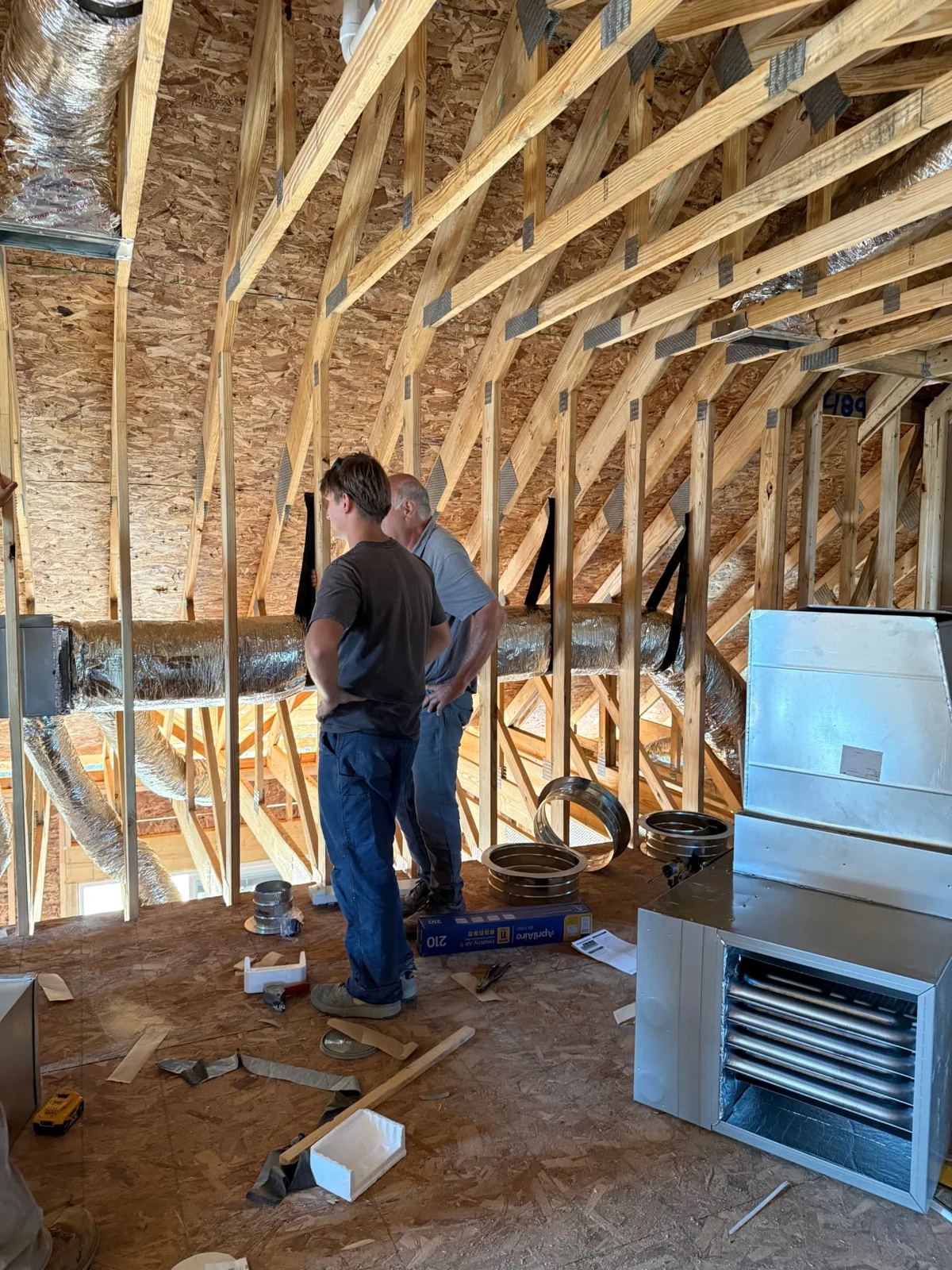 Brad and Kyle Sterchi inside a Sterchi home under construction, surrounded by framing and mechanical systems.